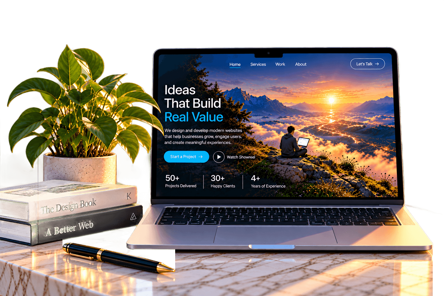 A laptop on a marble desk showing a modern agency website, beside a potted plant, design books and a pen